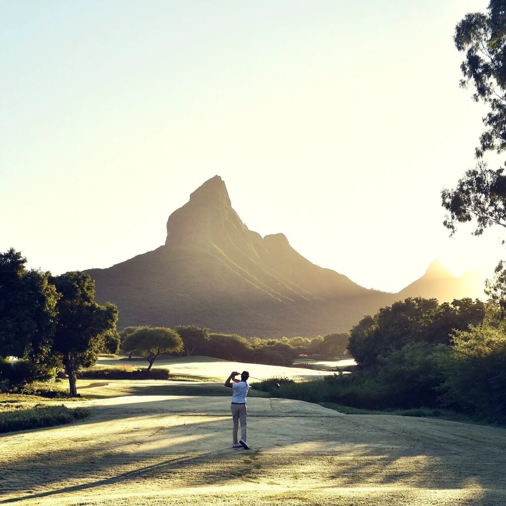 Golfer teeing off at sunrise beneath a Mauritian mountain